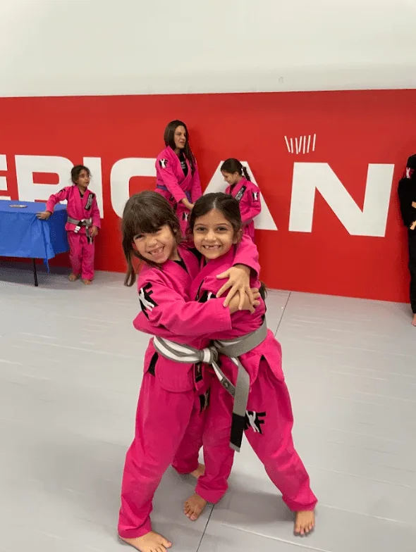 Young Brazilian Jiu-jitsu students in pink uniforms sharing a joyful moment